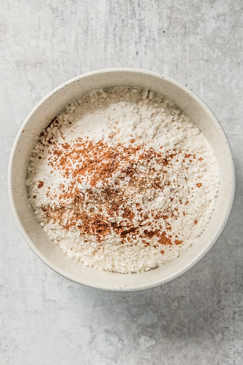 Spices and dry ingredients sit in a white ceramic bowl on a gray surface.