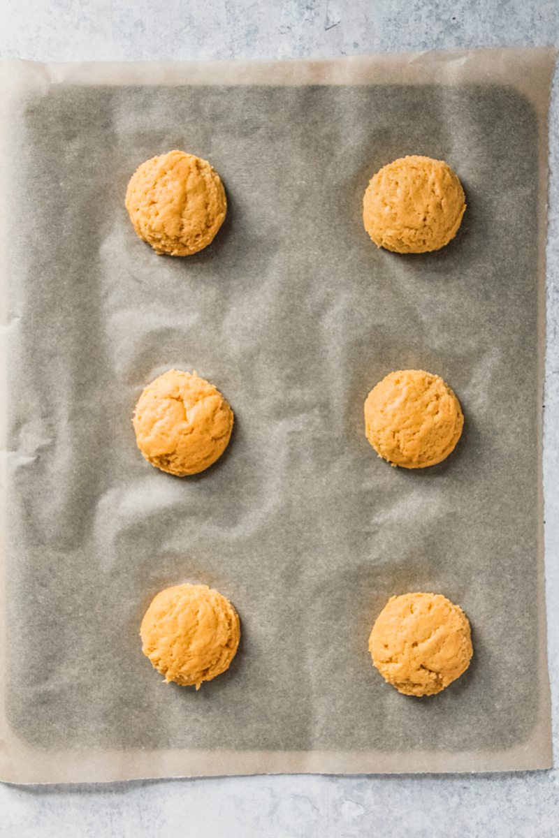 Unbaked pumpkin sugar cookies sit on a lined baking tray.