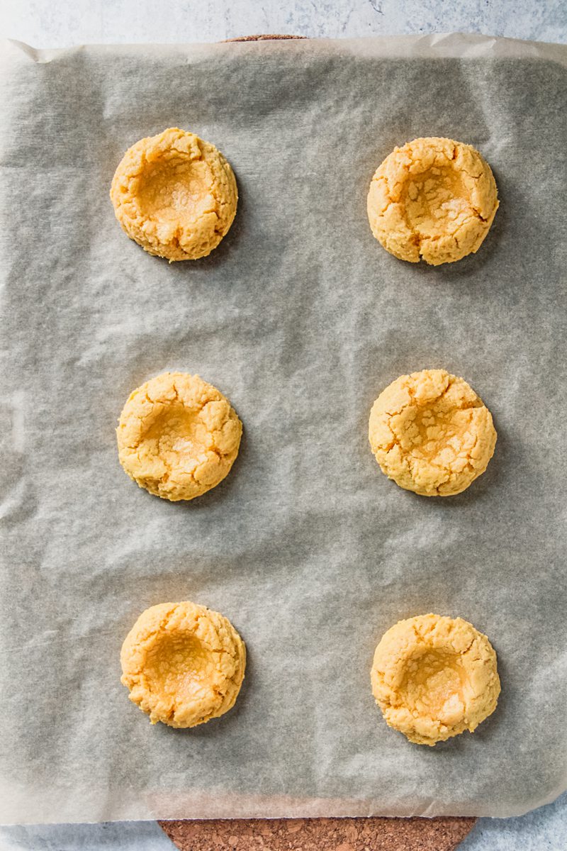 Baked pumpkin sugar cookies sit on a lined baking tray with an indent in the center.