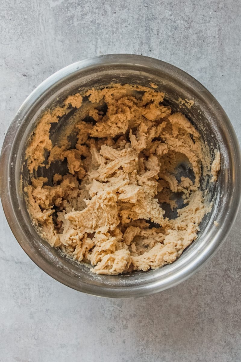 Cookie dough sits in a stainless steel bowl on a light grey surface.