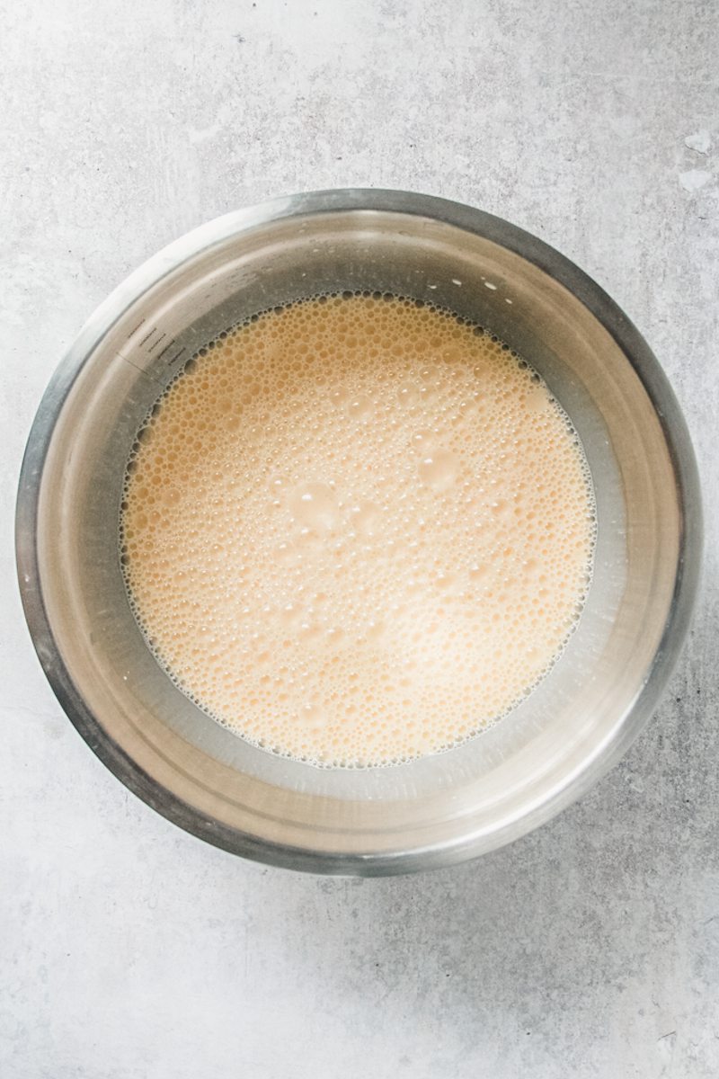 Flan custard mixture sits in a stainless steel bowl on a gray surface.