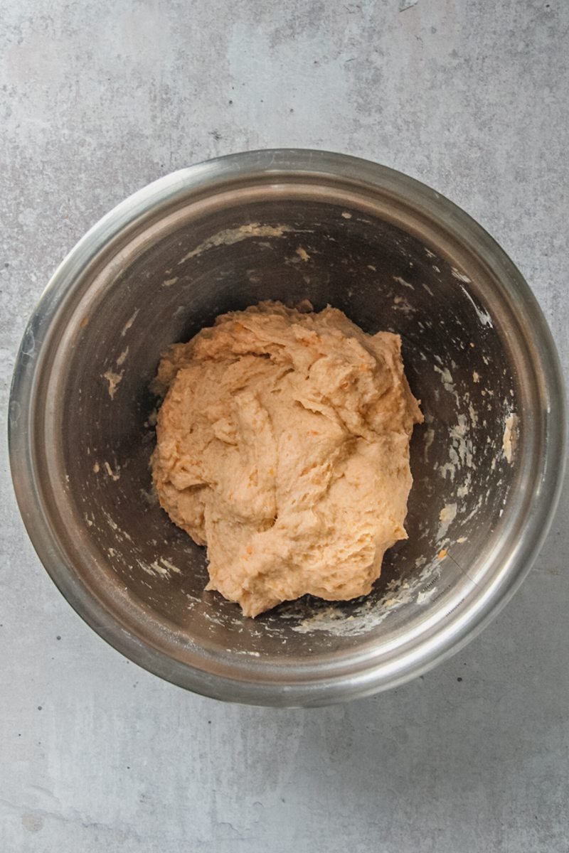 Sweet potato dough in a stainless steel bowl on a gray surface.