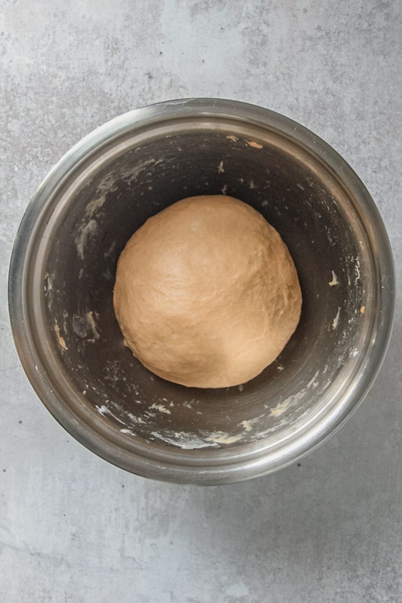 Rested sweet potato babka dough sits in a stainless steel bowl on a gray surface.