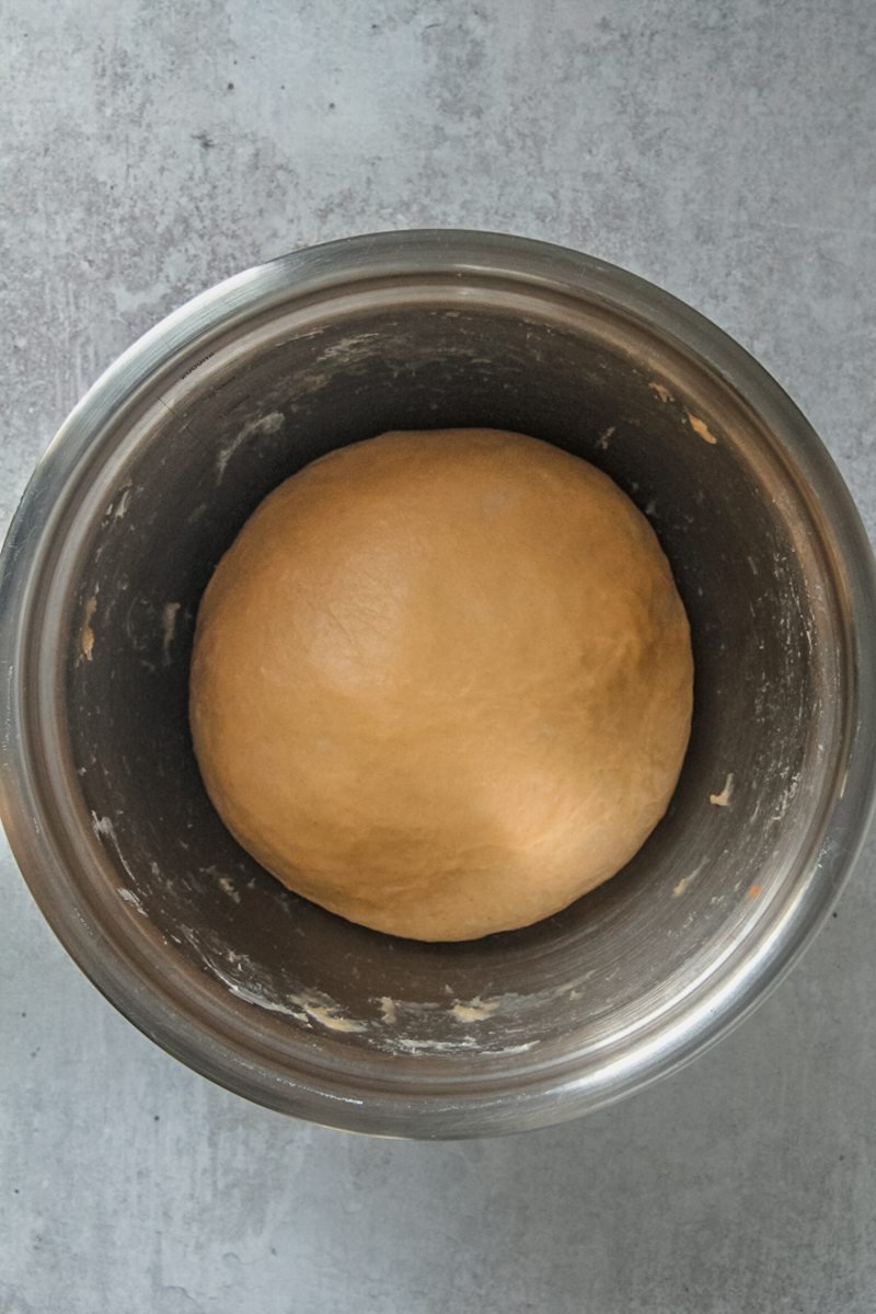 Risen sweet potato babka dough sits in a stainless steel bowl on a gray surface.