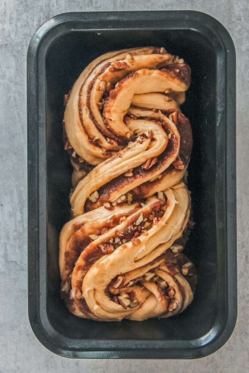 Swirls of folded sweet potato dough sits in a rectangle loaf tin on a gray surface.