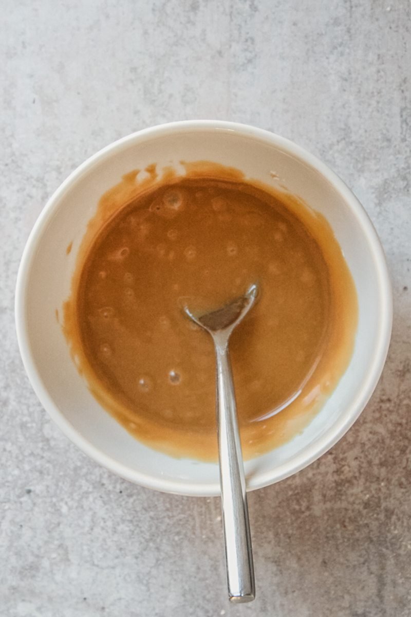 A coffee glaze sits in a white ceramic dish on a gray surface.