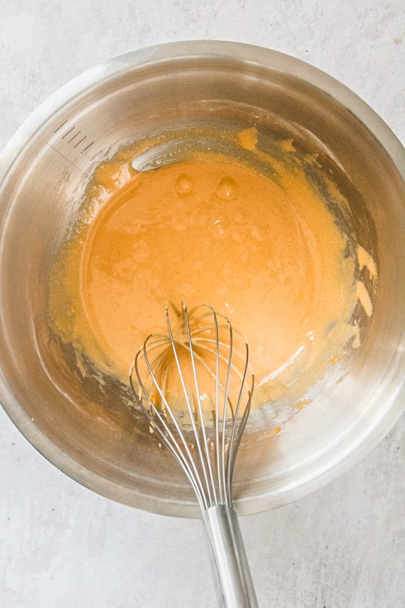 A brown sugar and egg yolk mixture sits in a stainless steel bowl on a gray surface.