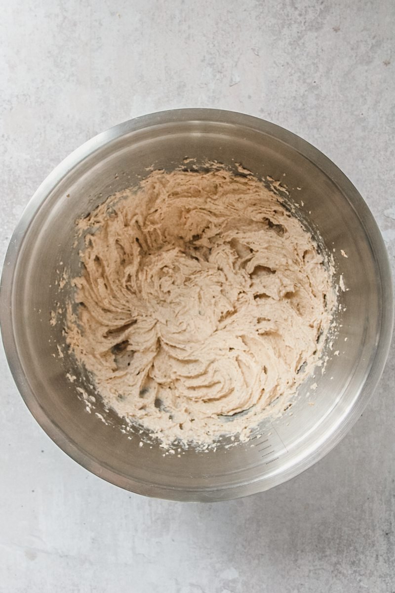 Whipped sugar and brown butter sit in a stainless steel bowl on a gray surface.