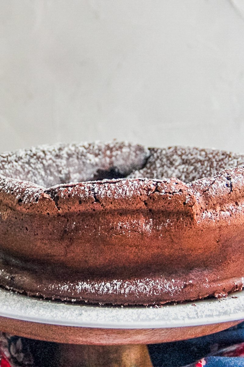 A close up of flourless chocolate cake sitting on a cake stand topped with powdered sugar.