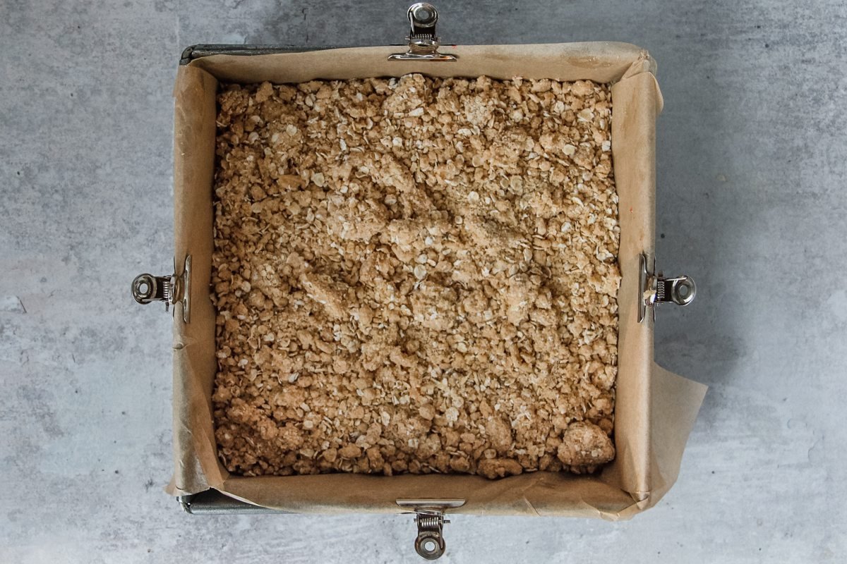 A streusel bar mixture sits in a square tin on a light grey background.