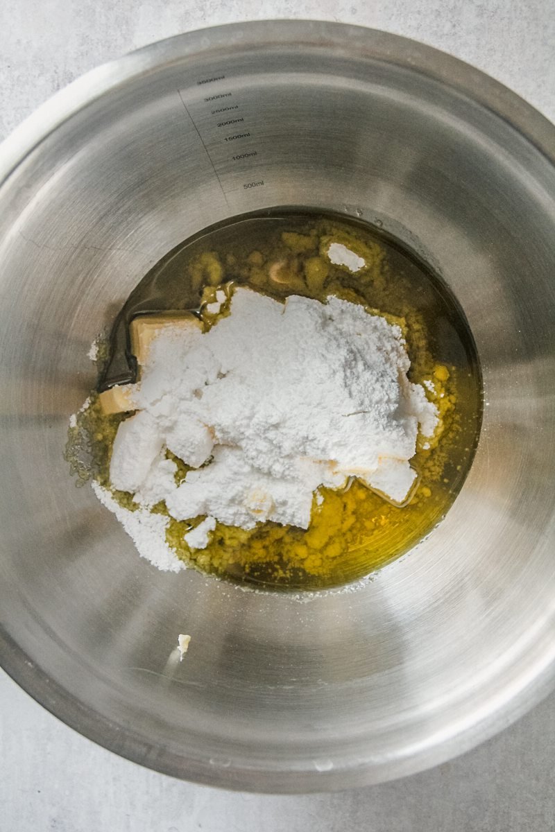 Olive oil, butter and powdered sugar sit in a stainless steel bowl on a gray surface.