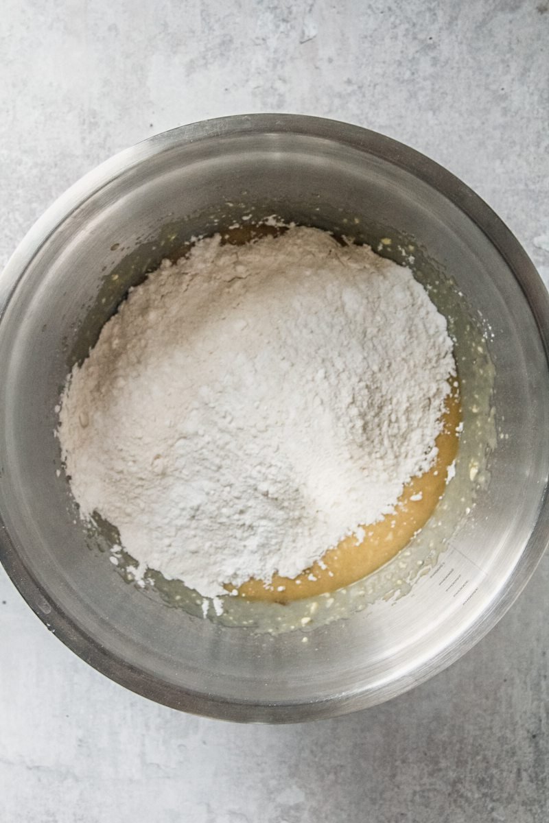 Dry ingredients sit on top of moist ingredients in a stainless steel bowl on a gray surface.