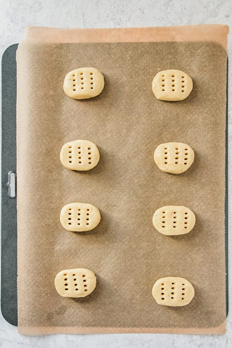 Pierced Greek walnut cookies sit on a parchment lined baking tray on a gray surface.