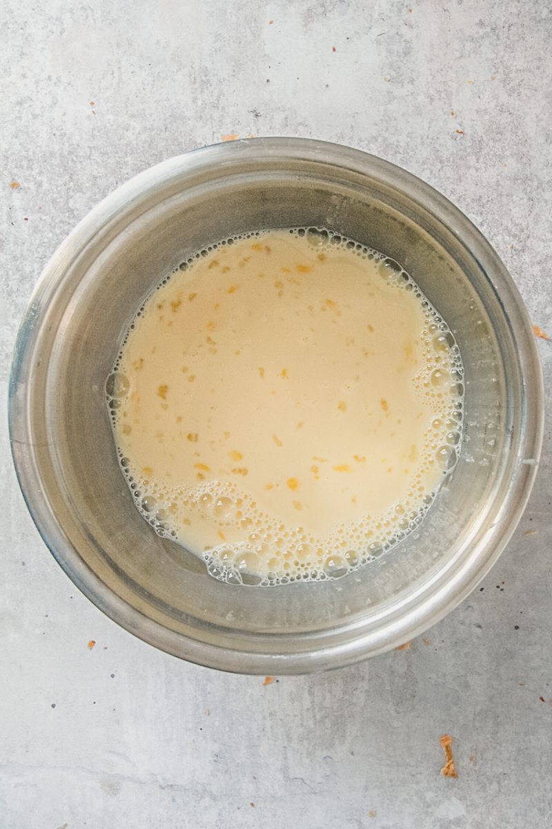 A French toast custard mixture sits in a stainless steel saucepan on a gray surface.