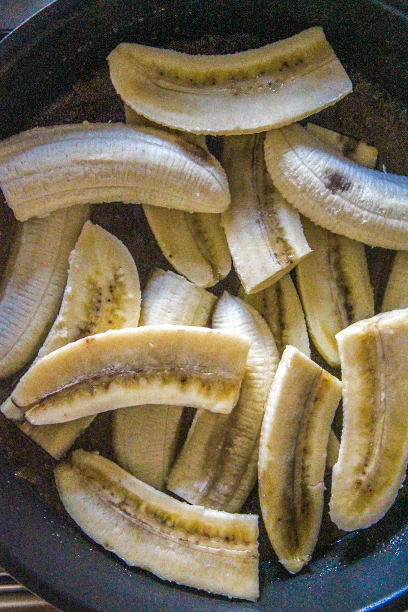Bananas sit on top of a caramel mixture in a saucepan.