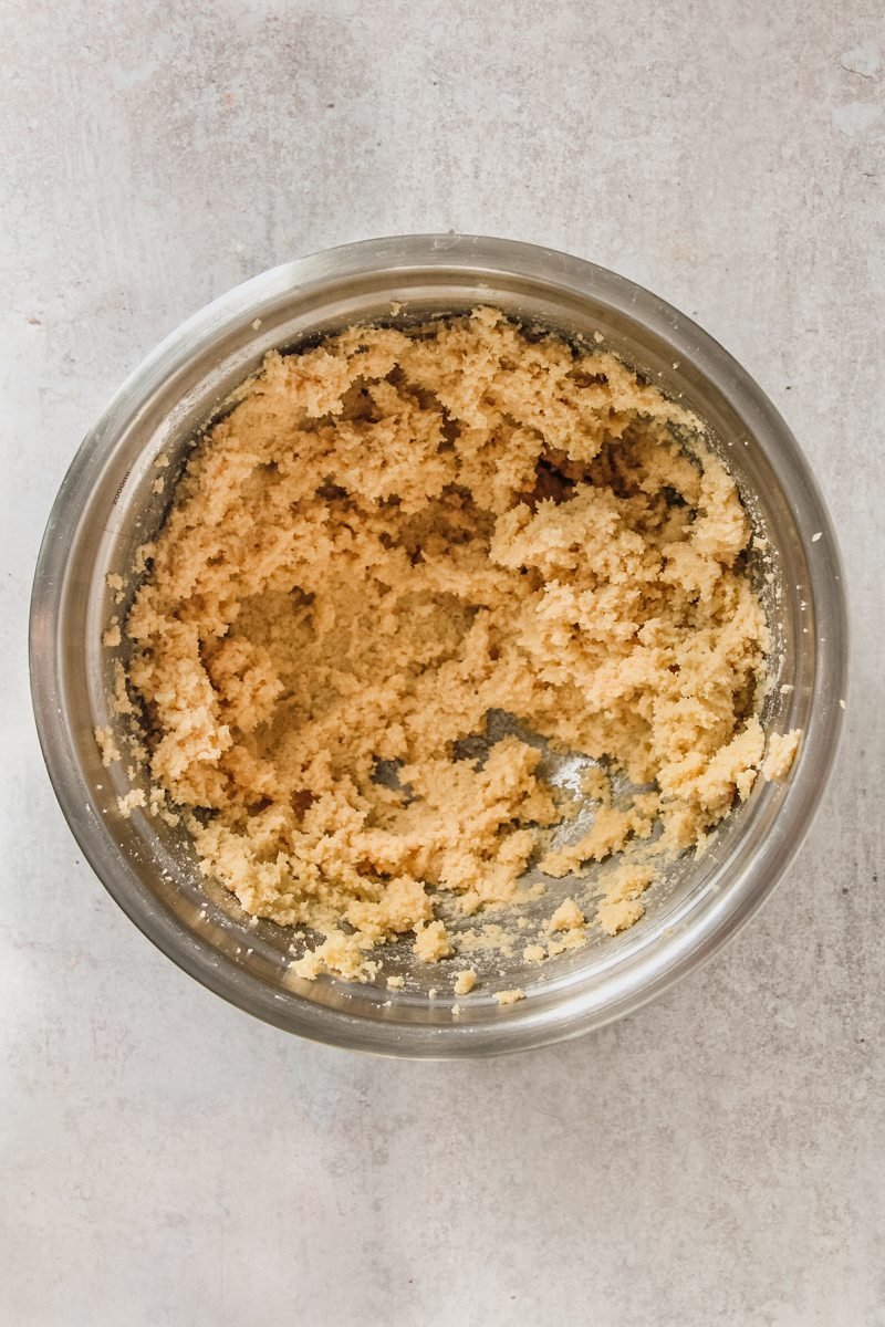 Whipped butter and almonds sit in a stainless steel bowl on a gray surface.