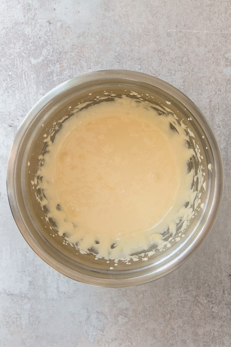 Whipped egg yolks sit in a stainless steel bowl on a gray surface.