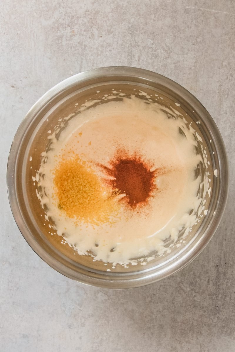 Fine lemon peel and ground cinnamon sit in a stainless steel bowl on a gray surface.