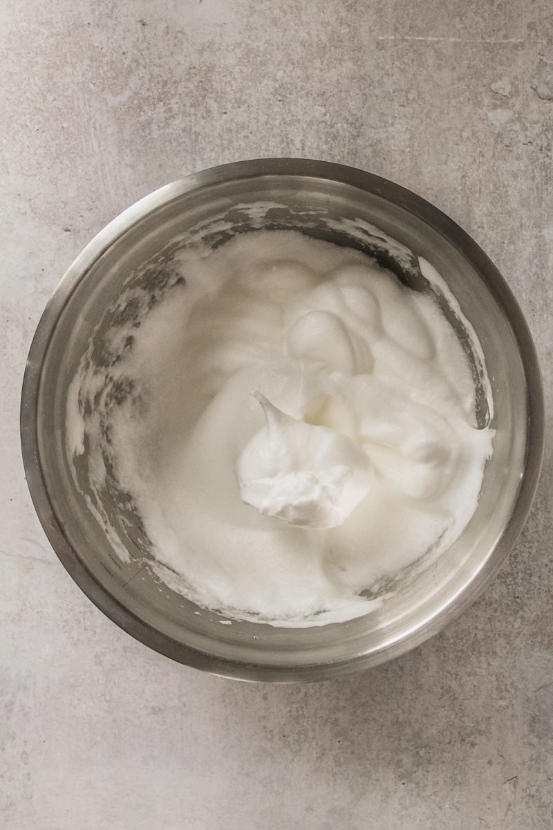 Egg whites sit in a stainless steel bowl on a gray surface.