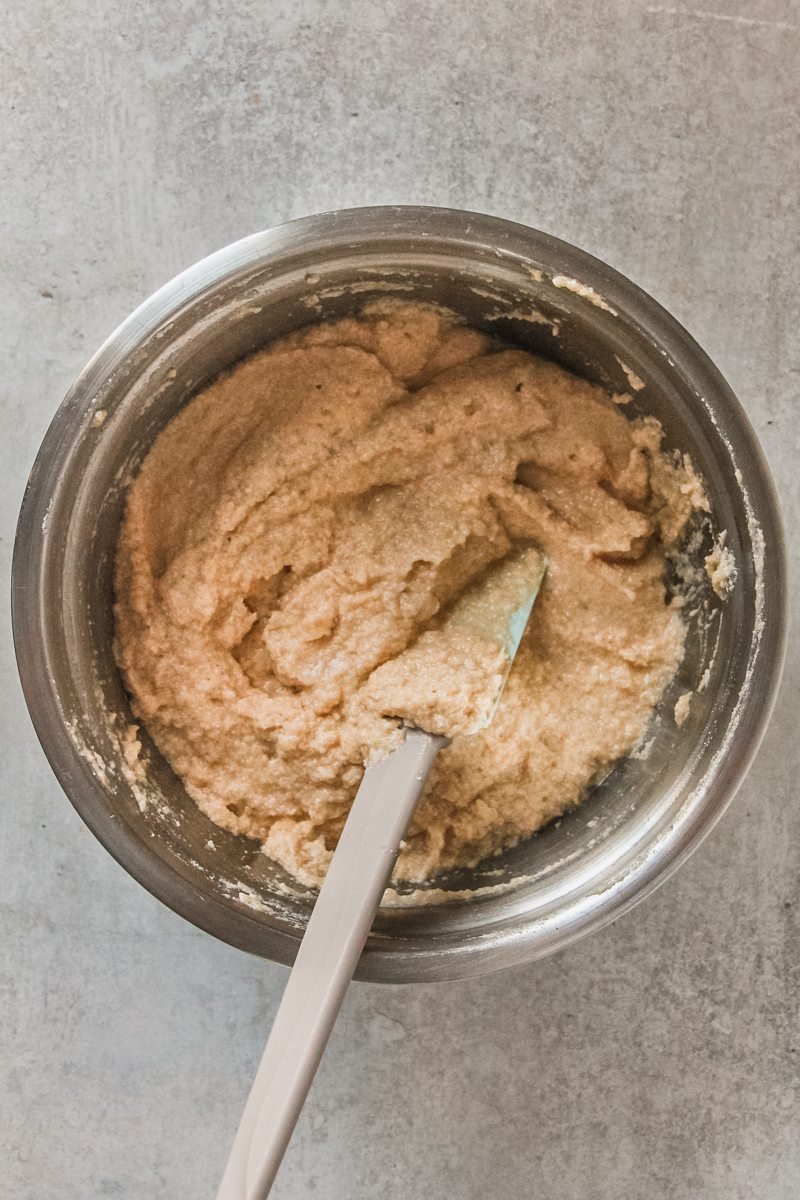 An almond flour and egg mixture sits in a stainless steel bowl on a gray surface.