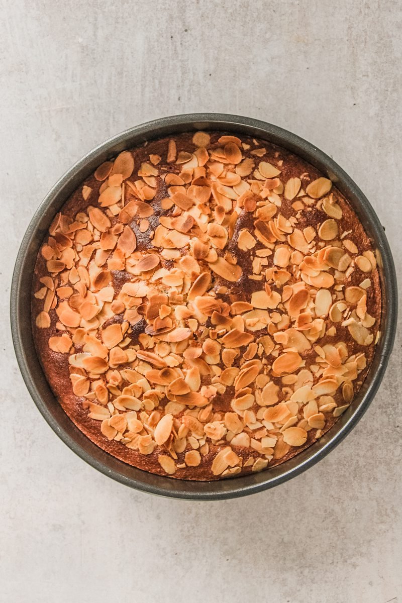 A baked Portuguese almond cake sits in a cake tin on a gray surface.