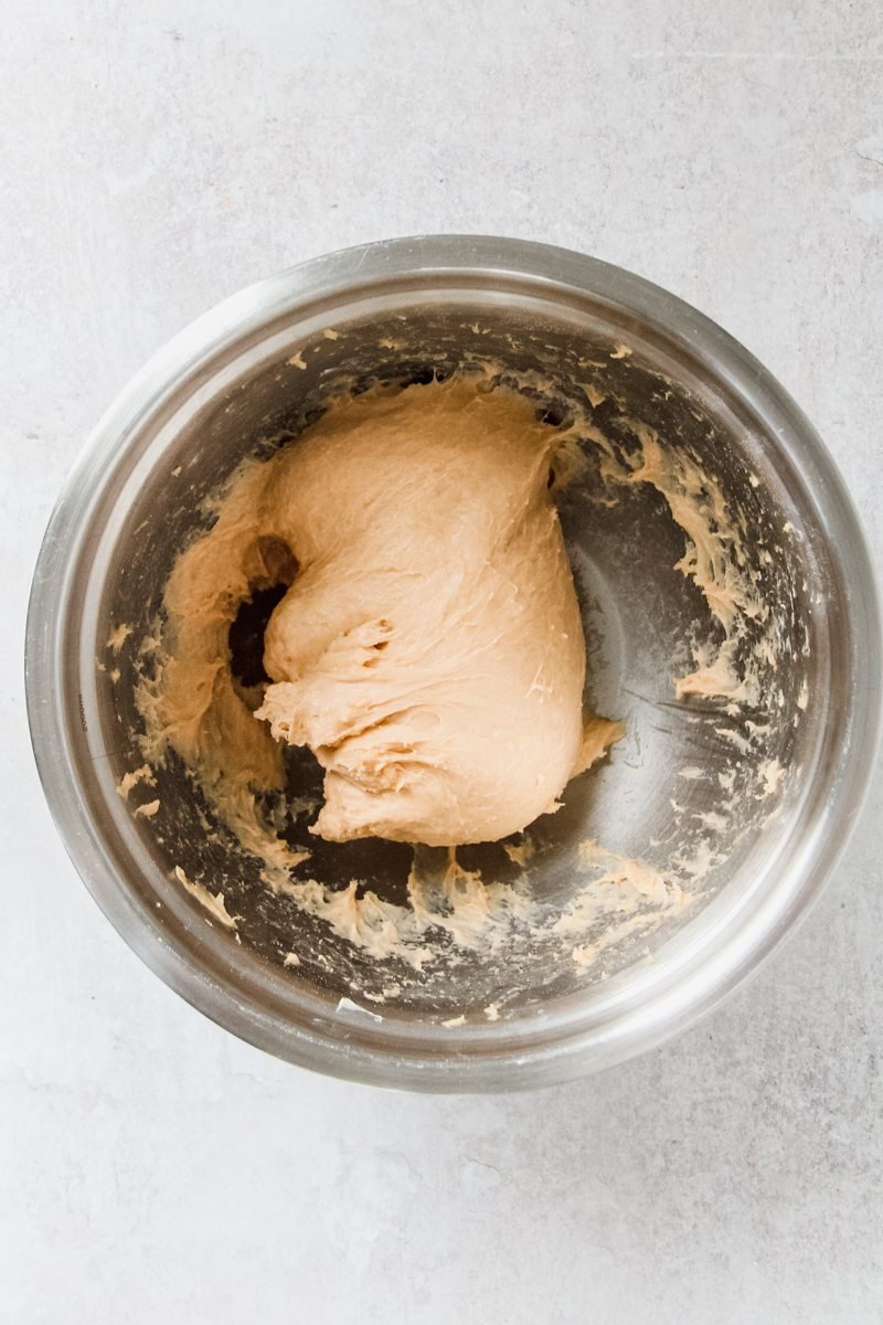 A fluffy brioche style dough sits in a stainless steel bowl on a gray surface.