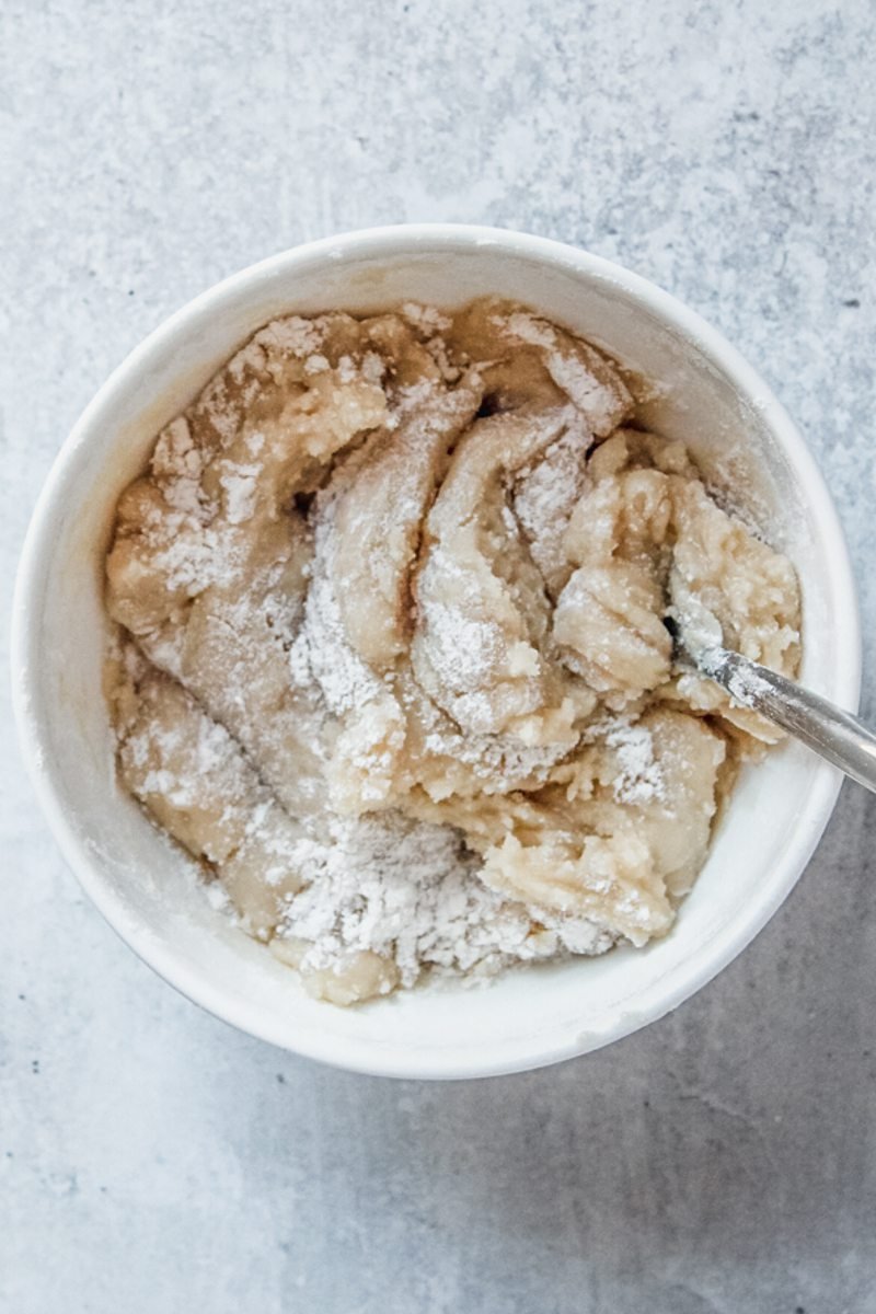 A honey and olive oil crumble or streusel mixture sits in a white ceramic bowl on a gray surface.