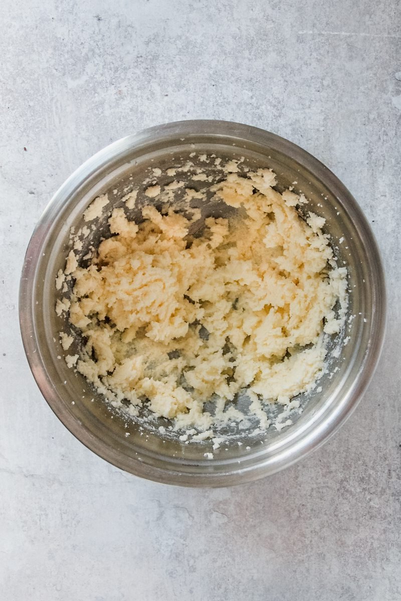 Creamed butter and sugar sit in a stainless steel bowl on a light grey surface.