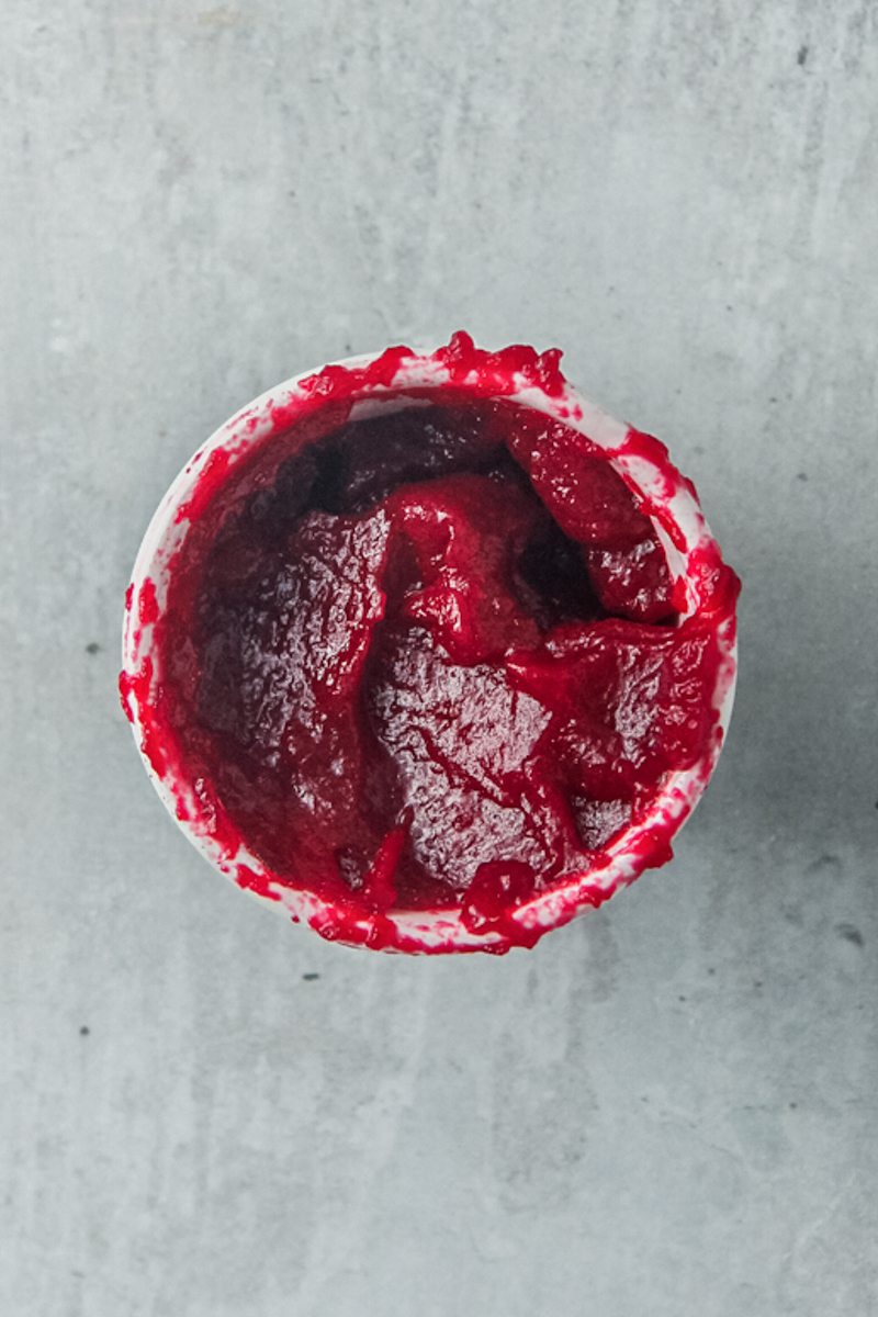 Cranberry puree sits in a small white ceramic bowl on a gray surface.