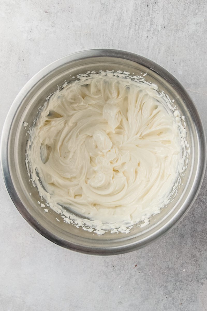 Whipped cream cheese sits in a stainless steel bowl on a gray surface.