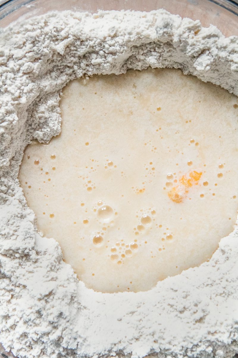 A buttermilk egg mixture sits in a crumbly dry mixture in a glass bowl on a wooden surface.