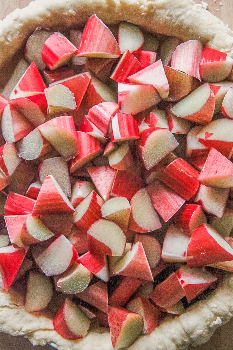 Chopped rhubarb sits inside a pastry base in a baking dish on a wooden surface.