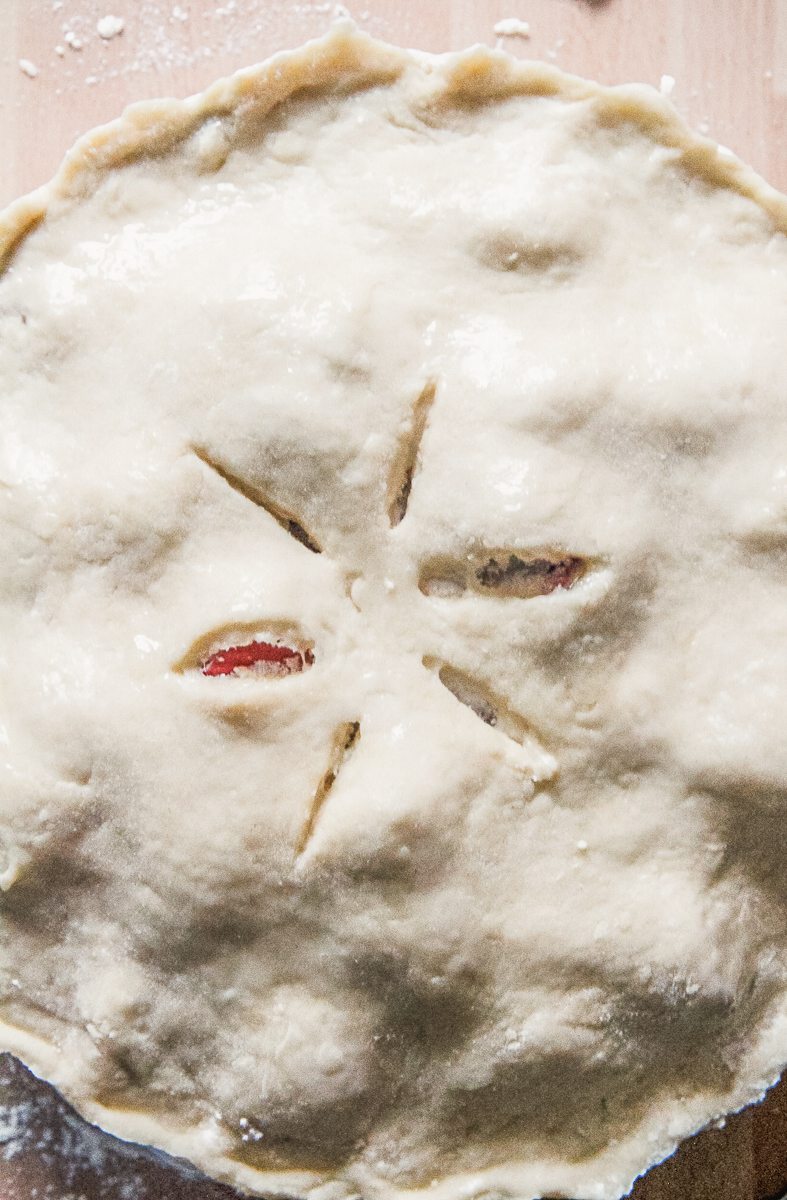 Slits marked into the top of a double crust pastry in a baking dish on a wooden surface.