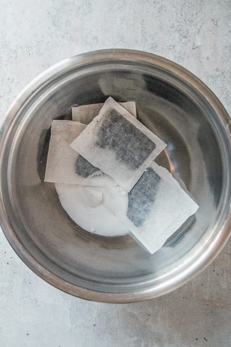 Tea bags and sugar sit in a stainless steel bowl on a gray surface.