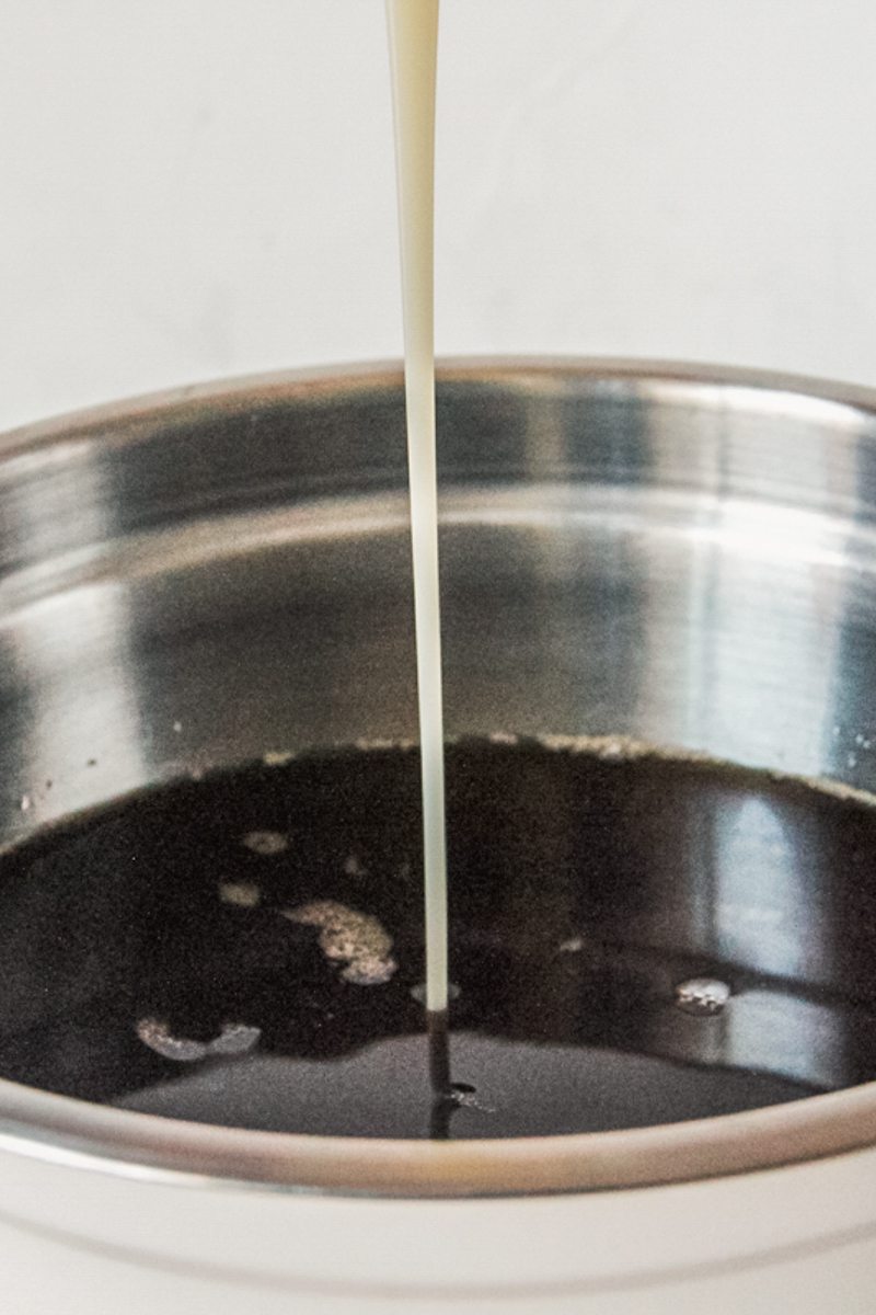 Sweetened condensed milk is poured into a tea mixture in a stainless steel bowl.