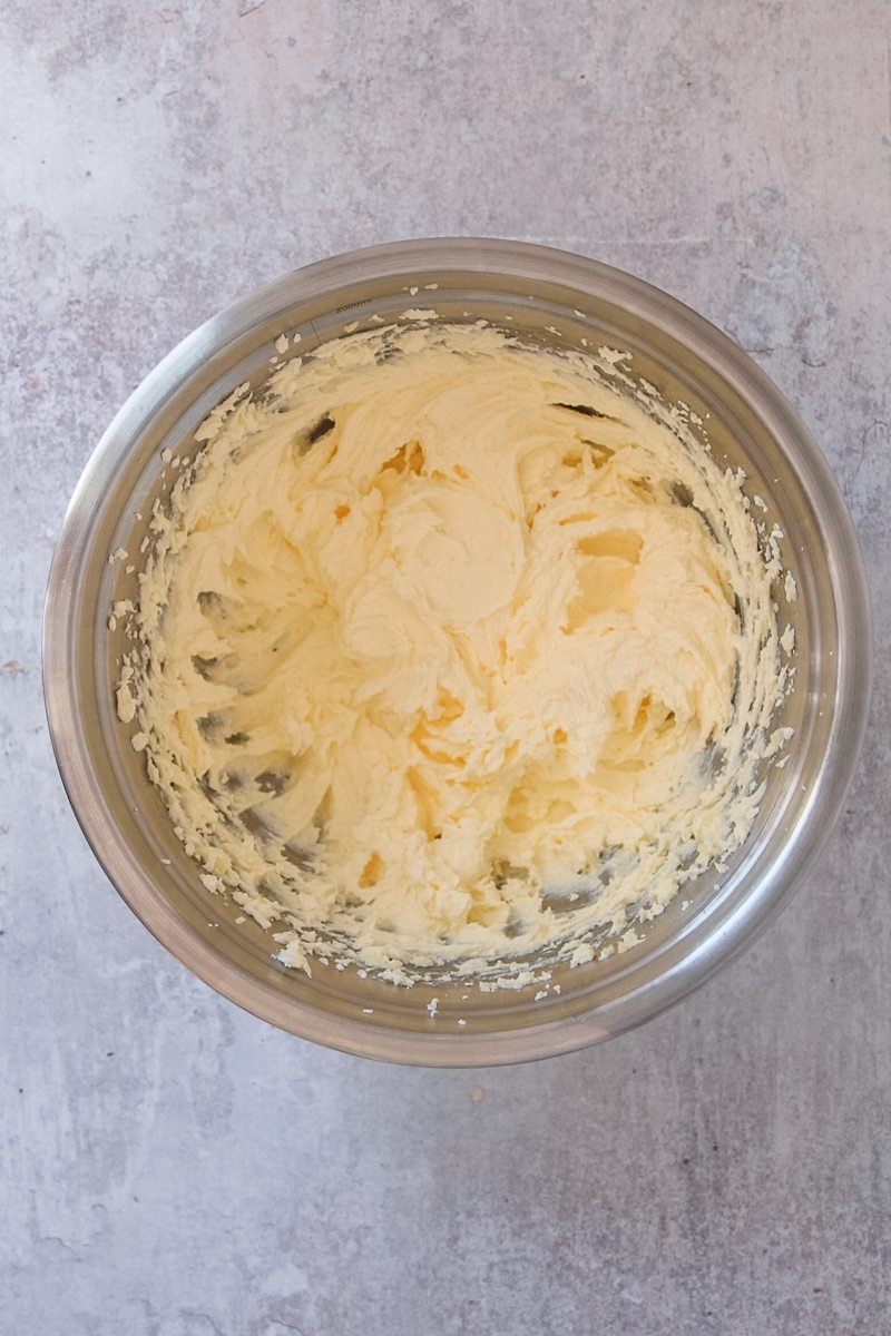 Whipped butter and sugar sit in a stainless steel bowl on a gray surface.