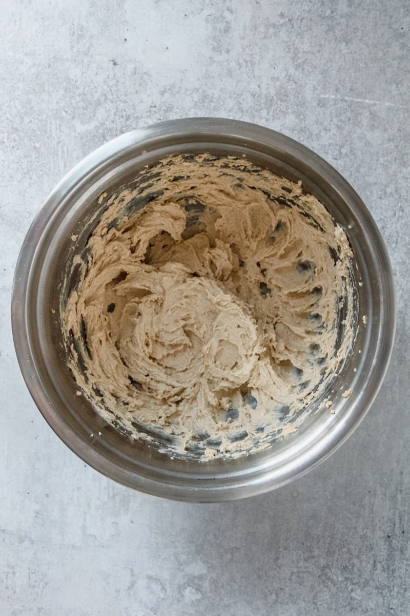 Muffin cookie dough sits in a stainless steel bowl on a light grey surface.