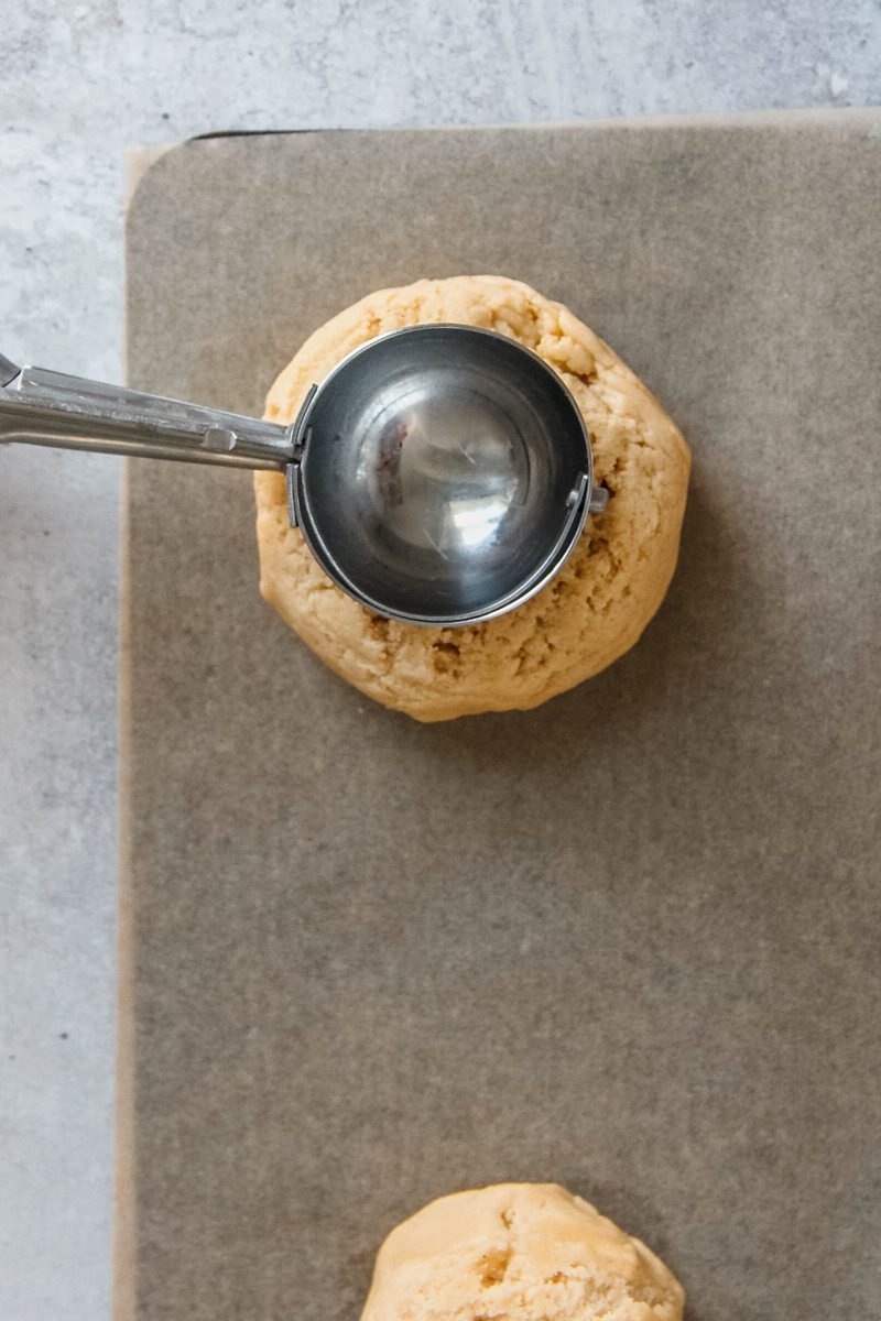 A deep indent is made into the center of muffin cookie dough on a baking tray.