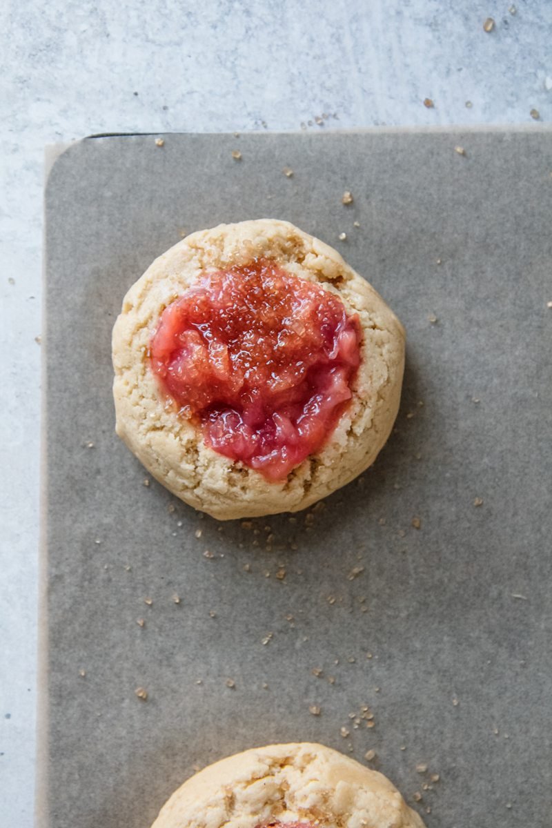 Peach jam sits in the center of cookie dough on a baking tray.