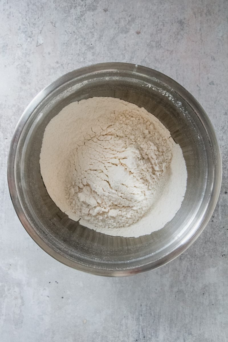 Dry ingredients sit sifted in a stainless steel bowl on a grey surface.