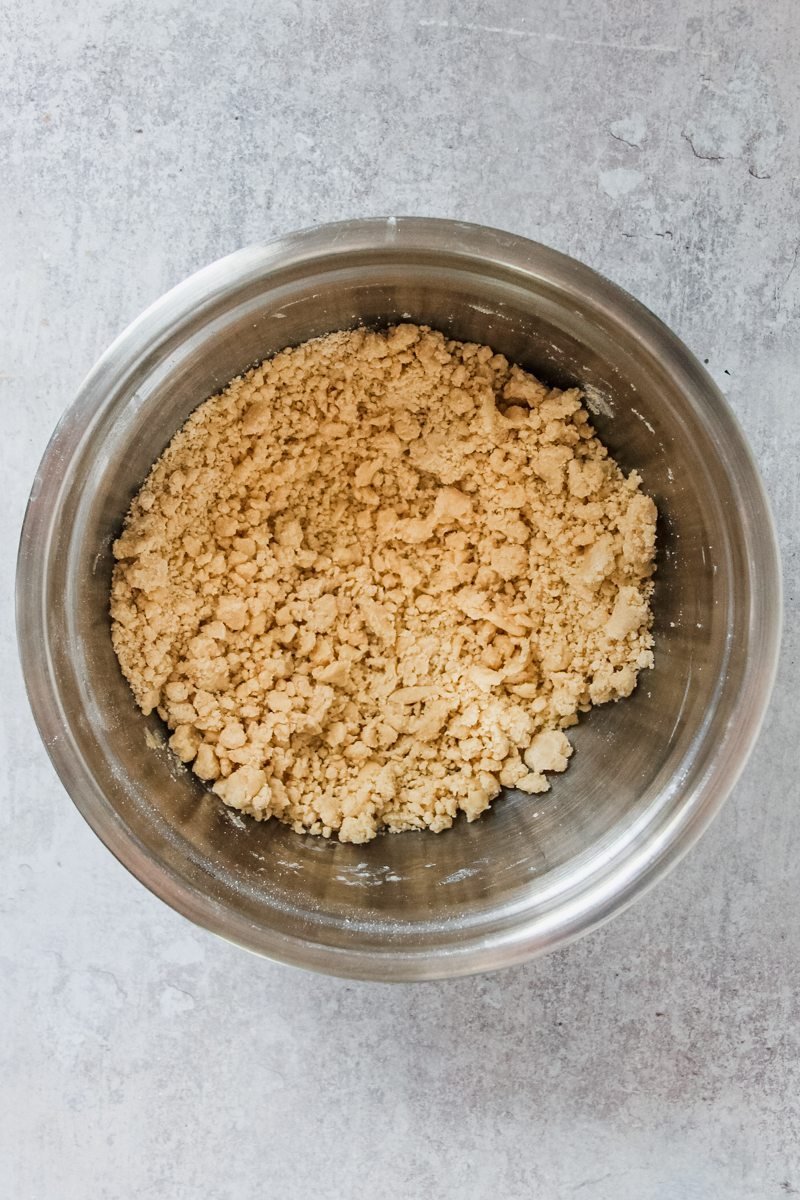 A rough breadcrumb mixture sits in a stainless steel bowl on a grey surface.