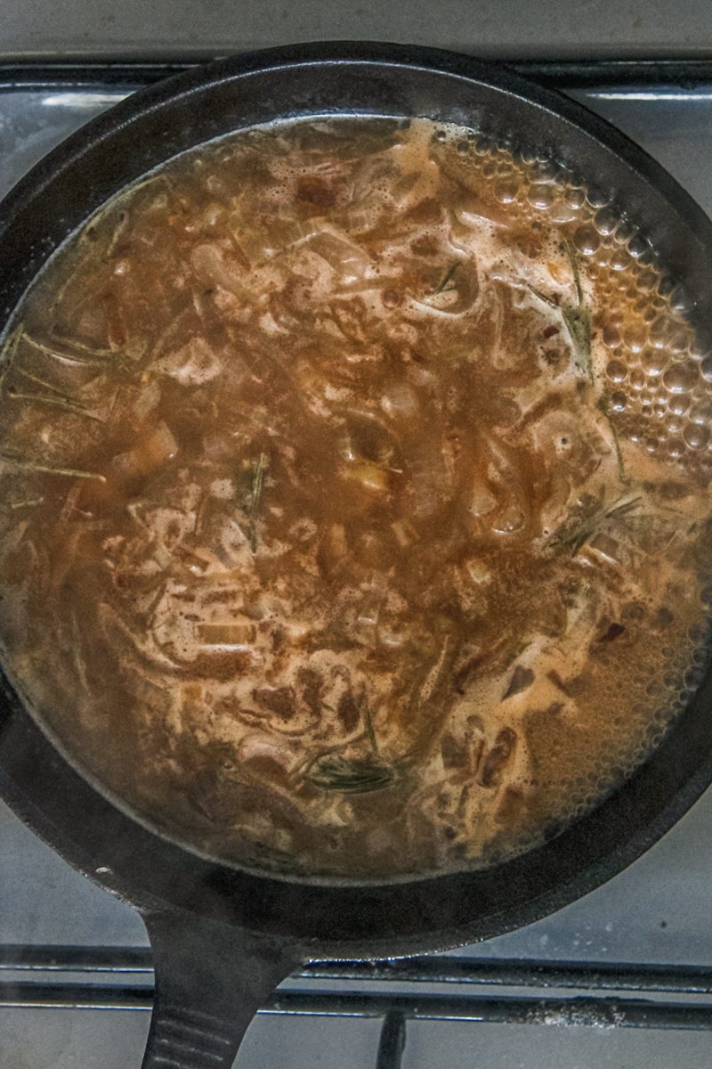 Beef gravy, rosemary and onions simmer in a cast iron skillet on a cooker.