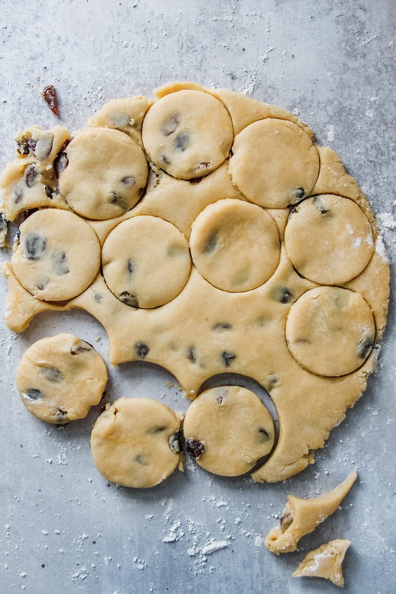 Round Welsh cakes are cut out of the dough on a grey surface.