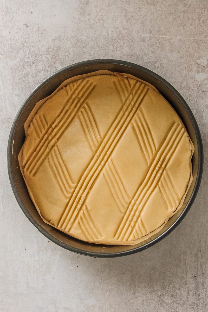 Dutch Butter Cake has fork tines marking on top in a round cake tin on a gray surface.