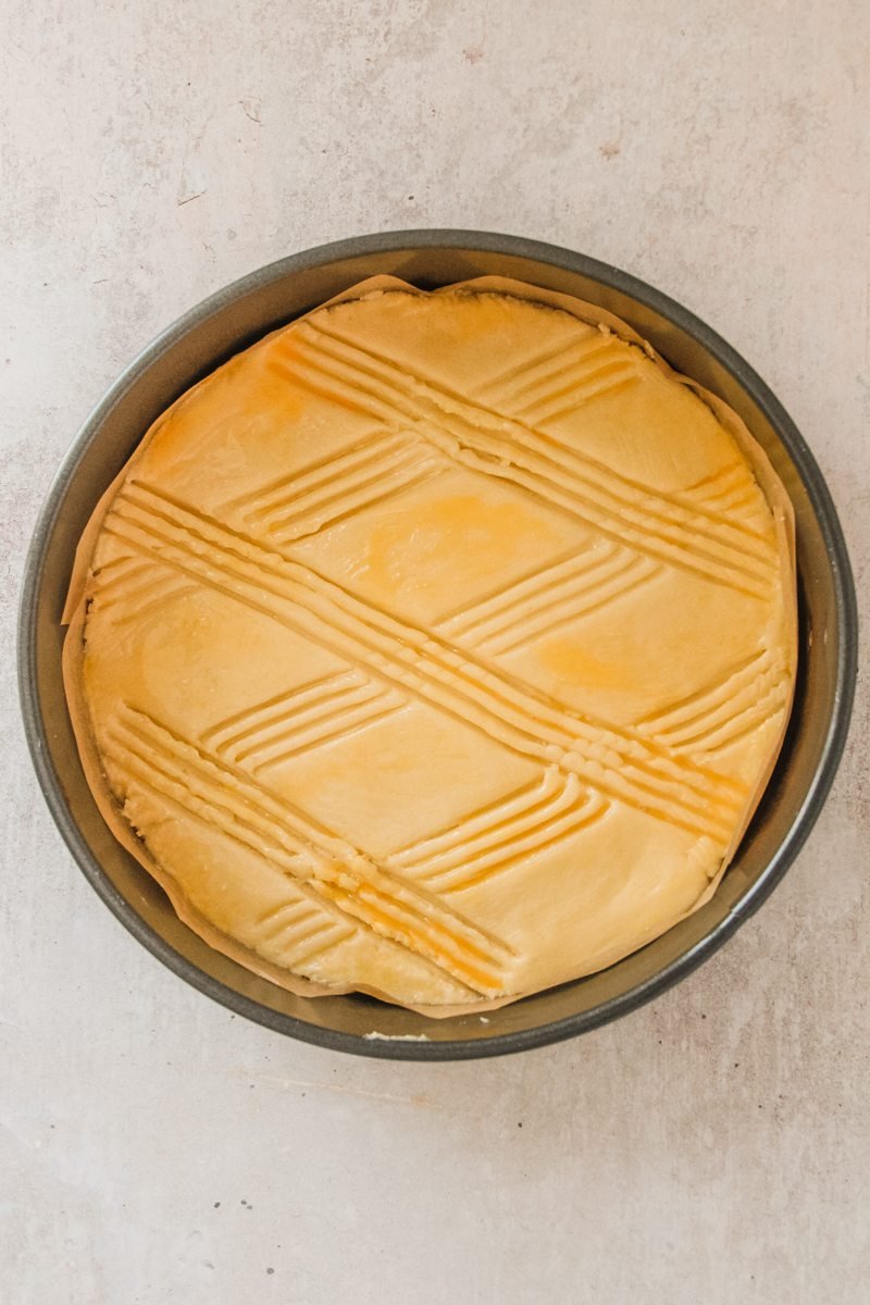 An unbaked Dutch butter cake sits in a round metal cake tin on a gray surface.