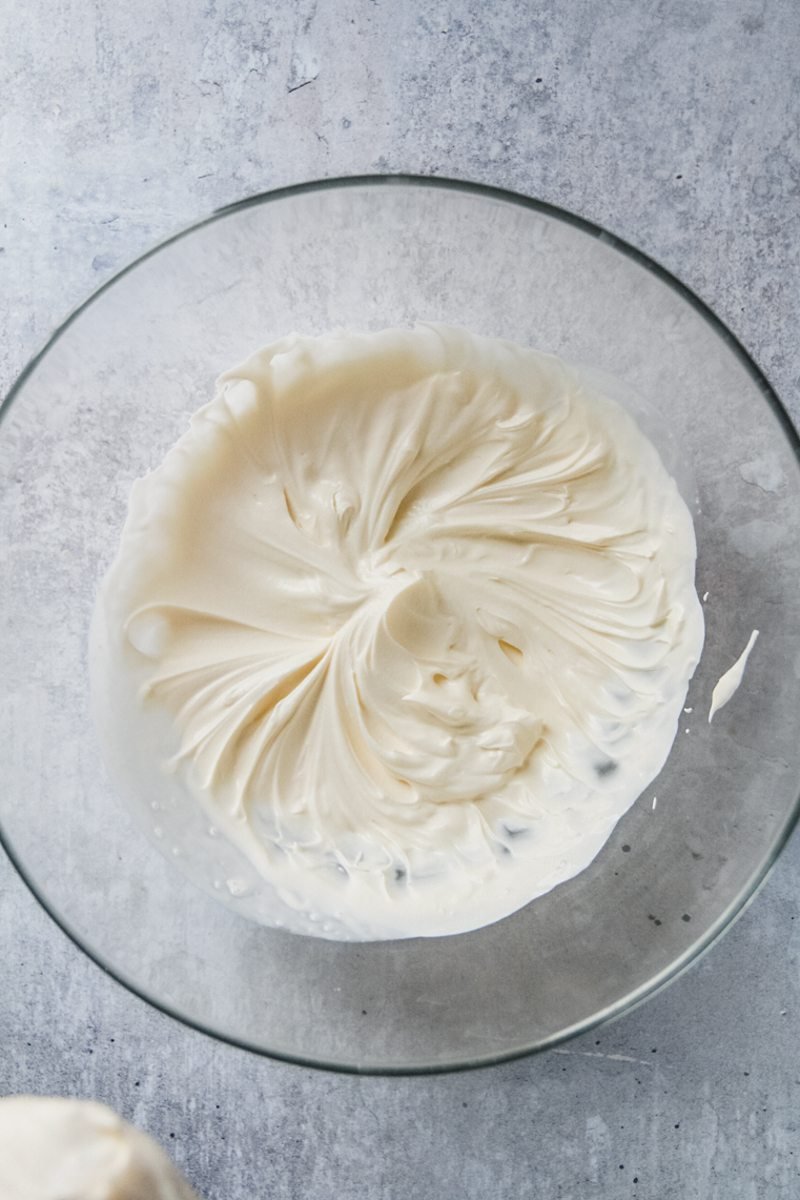 Whipped cream sits in a glass bowl on a gray surface.