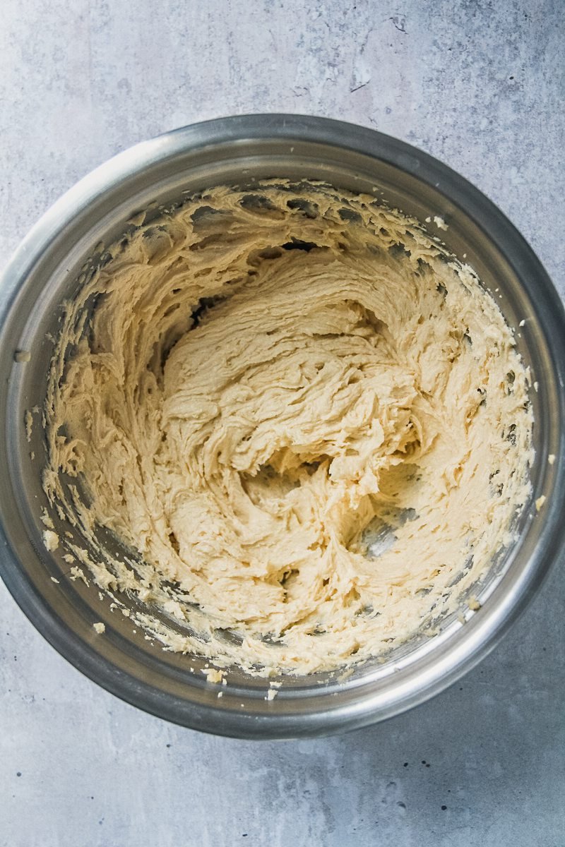 Whipped butter and eggs sit in a stainless steel bowl on a gray surface.