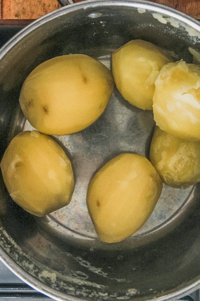 Cooked potatoes sit in a stainless steel saucepan on a cooker.