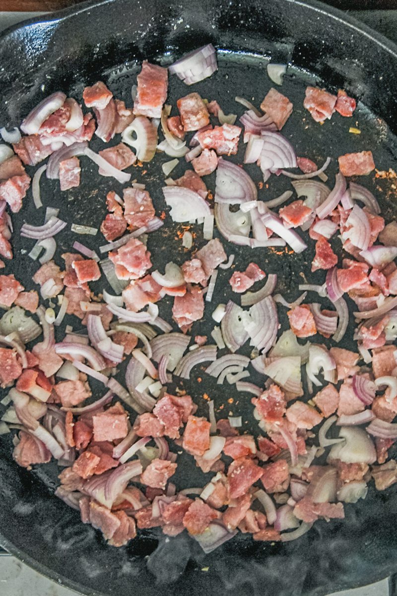 Roughly sliced onions sit in a cast iron skillet.