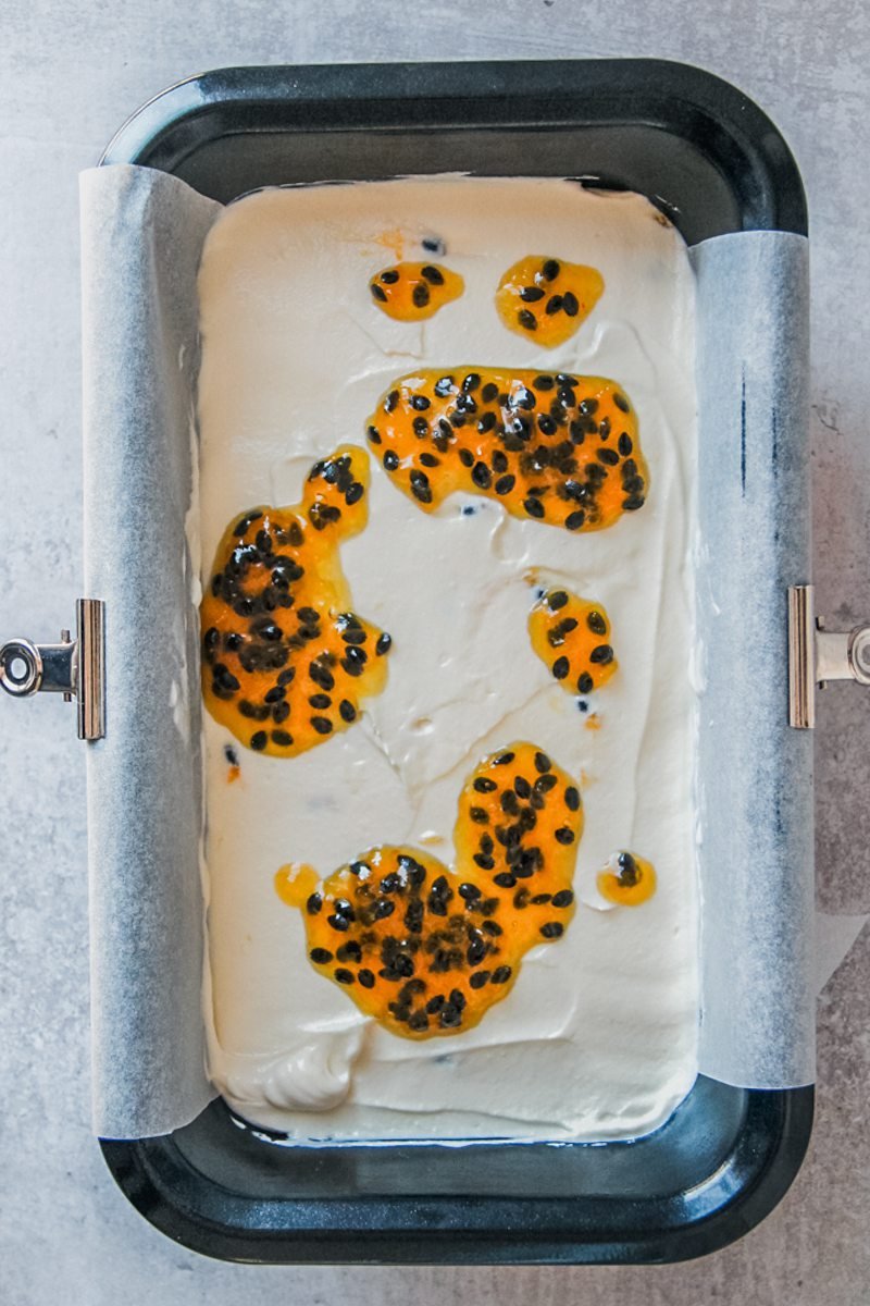 Cheesecake with passionfruit syrup on top sits in a lined metal loaf tin on a gray surface.